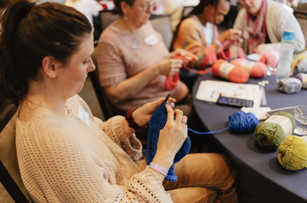 Beginner sample knitter knitting a pattern with yarn on the table.