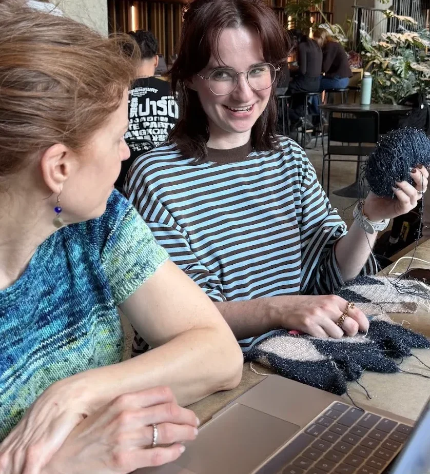 Maker community at a stitching circle meetup with a laptop and yarn, gathered around a table at a GoSadi knitting community event