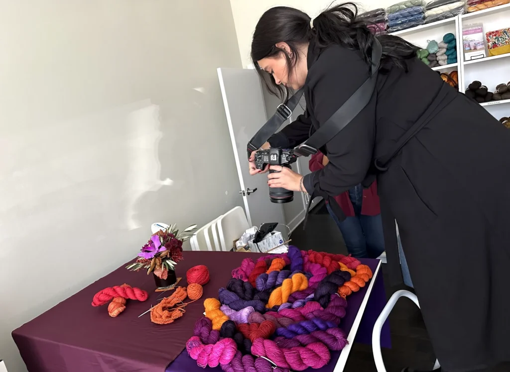 Professional product photography session at Nina Chicago yarn shop, with photographer capturing vibrant yarn colors including red, pink, orange, purple, and black skeins for e-commerce and marketing.