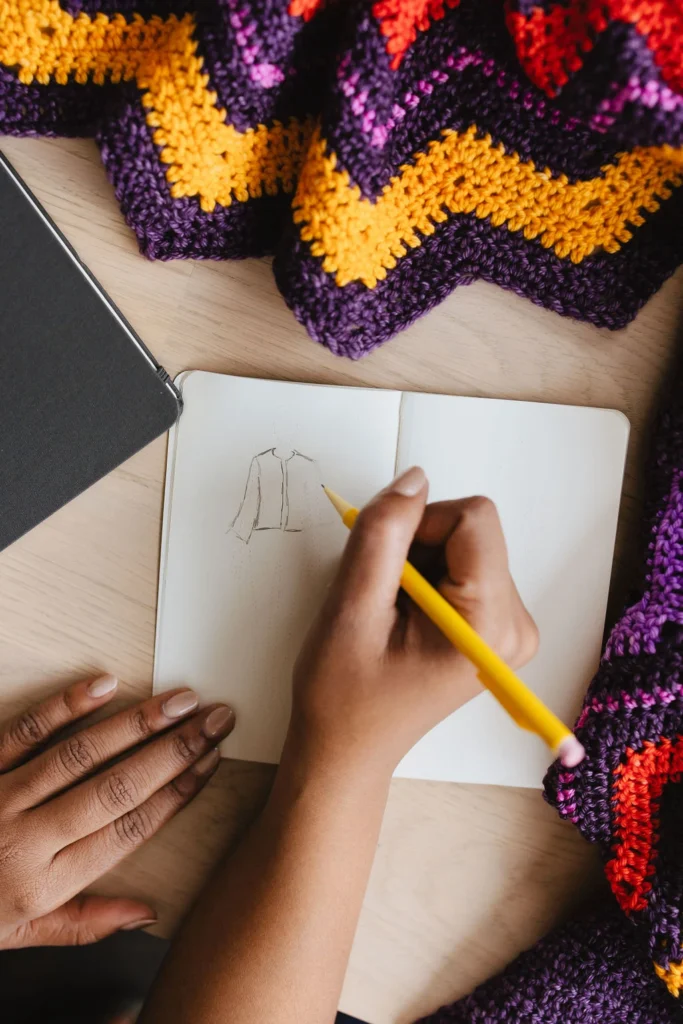 Designer drawing sketch in a notebook, surrounded by crochet samples
